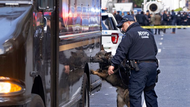 An NYPD canine officer and his dog sniffs a vehicle as an NYPD bomb disposal truck, background right, stands by on West&nbsp;58th Street next to the Time Warner Center after an explosive device was discovered in a mailroom Wednesday.