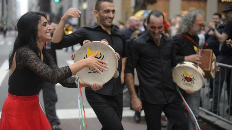 Performers dance with tambourines, coaxing onlookers to join in.