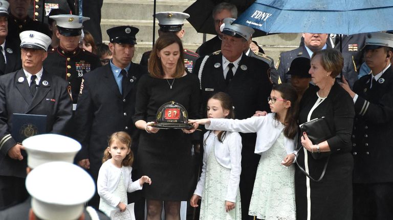 Still today, Americans die in service to the nation 2 Shannon Slutman, the wife of Christopher Slutman, holds her husband's helmet as their daughters (L to R) Wesleynn age 4, Kenley age 8 and McKenna age 10, touching hat, stand outside of St. Thomas Church in New York City at the conclusion of his funeral on April 26, 2019.