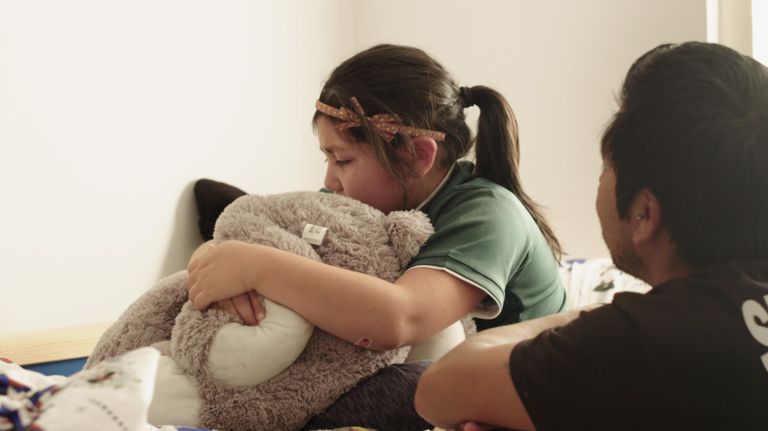 Sadie hugs a stuffed bear for comfort with her father, Jose Gonzalez, by her side.