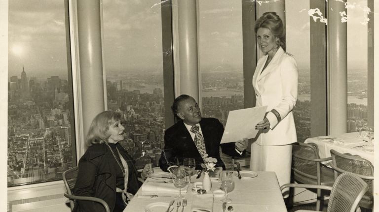 Guy Tozzoli, center, who oversaw construction of the World Trade Center, enjoys a meal at Windows on the World in 1976. Serving Tozzoli and his guest is Captain Claudette Fournier.