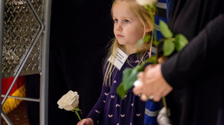 Aurora Folts, 3, granddaughter of firefighter Michael McDonald, holds a white rose during the World Trade Center Memorial Wall dedication ceremony at FDNY headquarters on Friday.