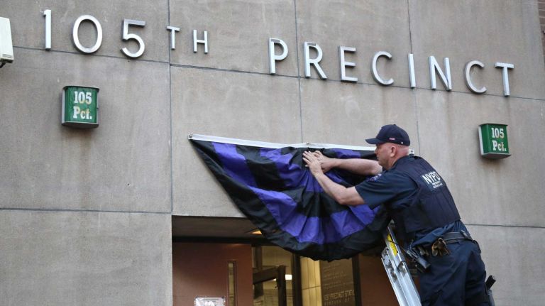 NYPD Emergency Service Officer Chris McNerney hangs the funeral bunting over the entrance to the 105th Precinct in Queens Village on Monday evening, May 4, 2015, in honor of NYPD Police Officer Brian Moore, 25, of Massapequa, who passed away from his injuries after being shot on Saturday, May 2.