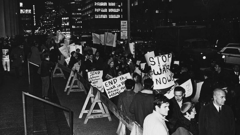 Long shot of anti-war pickets walking across from the Hilton Hotel with signs against Dean Rusk, who was to speak at Foreign Policy Association Dinner. (Nov. 14, 1967)