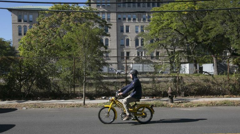 A man rides a moped past the now defunct Greenpoint Hospital. (Sept. 17, 2013)