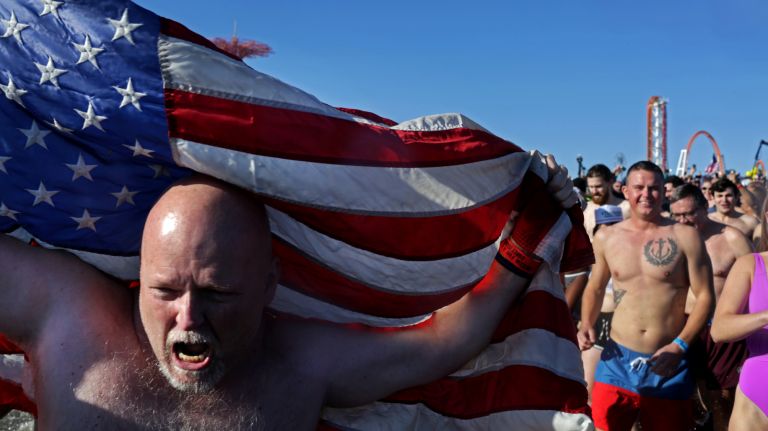 A man carries an American flag as he runs into the ocean during the Coney Island Polar Bear Club's New Year's Day Swim on Jan. 1, 2017.