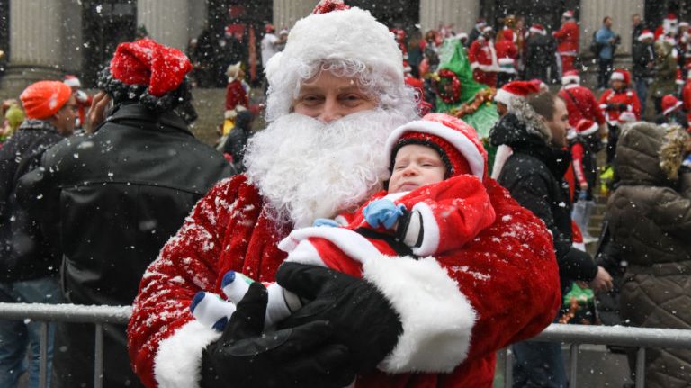 A bearded Santa keeps his baby bundled in his arms during SantaCon on Saturday, Dec. 9, 2017.