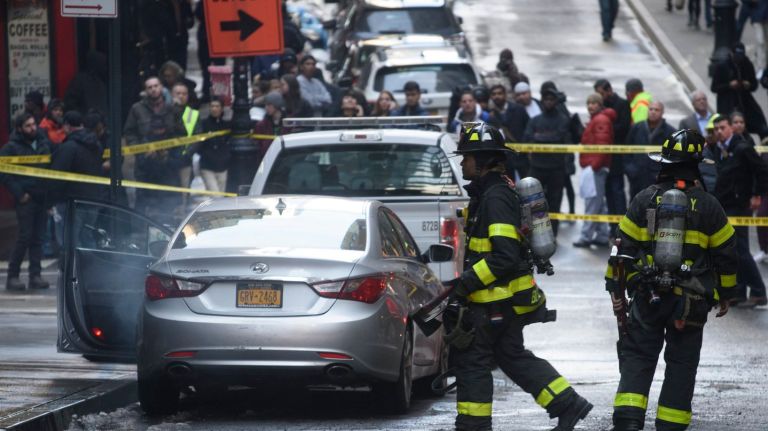 Firefighters walk past a smoking car after a manhole exploded on Nassau Street in Manhattan, Thursday, March 22, 2018. 