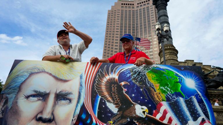 Creator of a Trump themed painting, Julian Raven of Elmira, New York, left, speaks with passersby about his inspiration for the work, as he stands with it in downtown Cleveland on the eve of the Republican National Convention in Cleveland, Ohio, on Sunday, July 17, 2016. Right is Bob Hayssen of upstate New York, a Republican delegate. Raven is an alternate delegate for the same region.