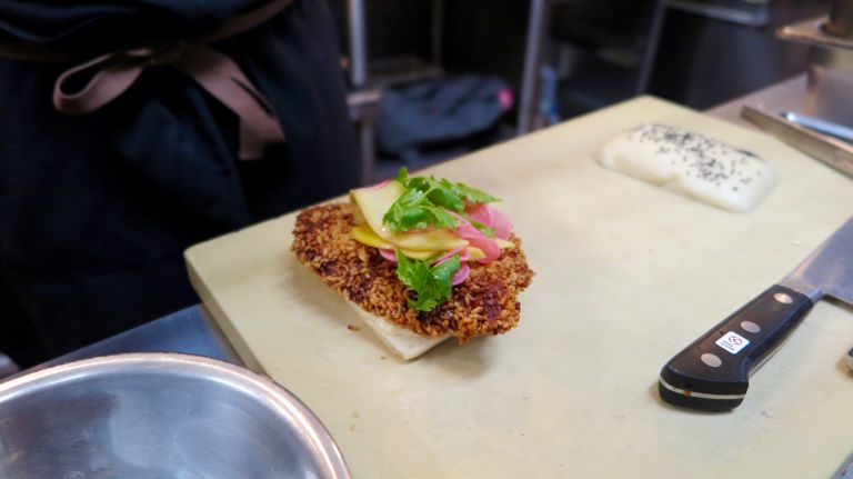 Once the chicken is fried, it's placed on the steamed bao bun with aioli and topped with green mangos, pickled radish and cilantro. 