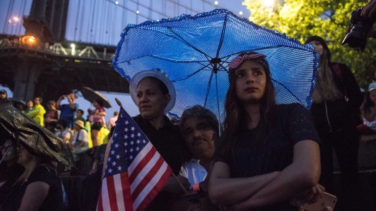 People wait in the rain to watch the Macy's 4th of July Fireworks from Brooklyn Bridge Park on July 4, 2016.