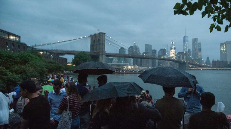 People wait in the rain to watch the Macy's 4th of July Fireworks from Brooklyn Bridge Park on July 4, 2016.