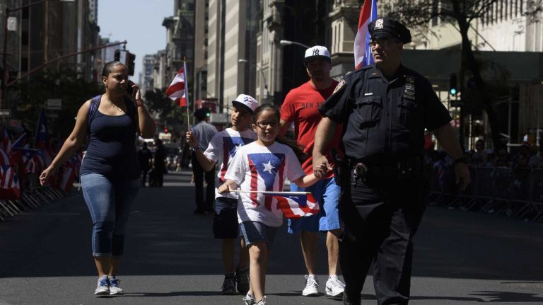 A police officer holds a child's hand as they walk on Fifth Avenue before the start of the Puerto Rican Day Parade in Manhattan on Sunday, June 12, 2016.