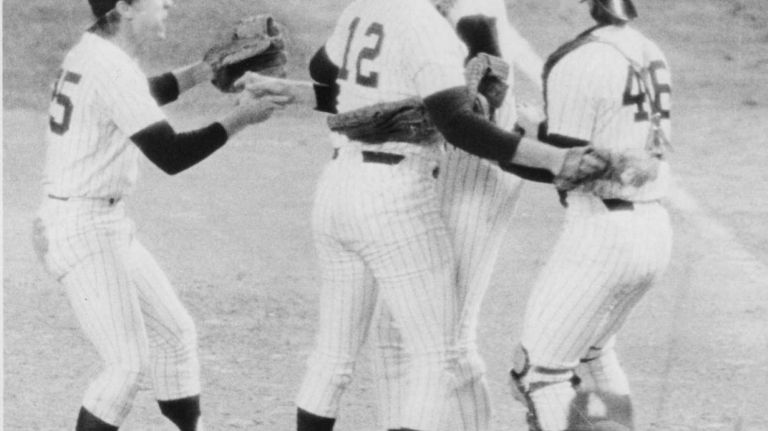 Yankees' Jim Spencer, No. 12, hugs rookie pitcher Jim Beattie, and is joined by infielder Brian Doyle, left, and backup catcher Mike Heath, right, to celebrate the team's win in Game 5 of the World Series at Yankee Stadium on Oct. 15, 1978. The Yankees would win the Series in Game 6 against the Los Angeles Dodgers at Dodger Stadium two days later.