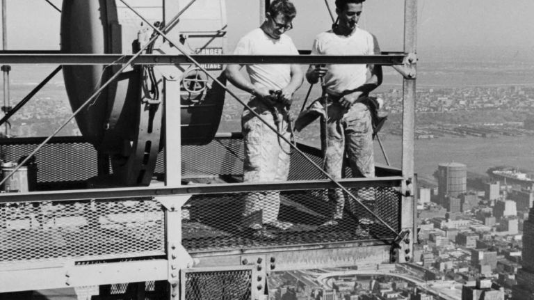 Jack Engleman, of the Bronx, and Harry Dane, of Bayside, Queens, begin work painting the tower of the Empire State Building on Aug. 2, 1962. The men are standing in an enclosure that houses one of the beacon lights adorning the skyscraper.