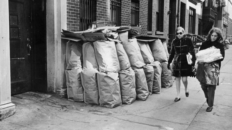 Women walk past stacks of garbage on West 11th Street during the sanitation strike on Feb. 5, 1968.