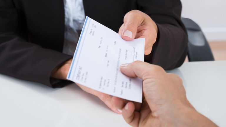 Close-up Of Businessperson Hands Giving Cheque To Other Person At Desk