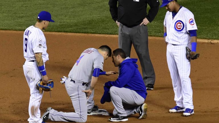 New York Mets trainer Ray Ramirez tends to New York Mets shortstop Wilmer Flores (4) after Chicago Cubs second baseman Javier Baez (9) came down on his head while stealing second base in the first inning during Game 4 of the NLCS against the Chicago Cubs at Wrigley Field on Wednesday, Oct. 21, 2015.