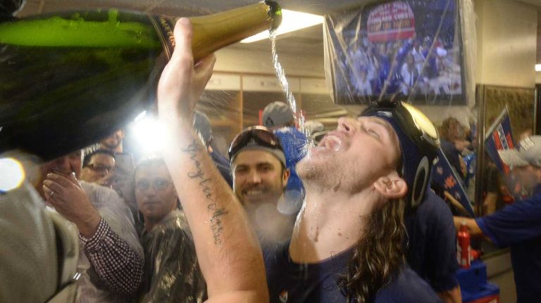 New York Mets starting pitcher Jonathon Niese (49) pours the big bottle of champagne into Mets starting pitcher Jacob deGrom's mouth as teammates celebrate in the clubhouse after beating the Chicago Cubs in the NLCS at Wrigley Field on Wednesday, Oct. 21, 2015.