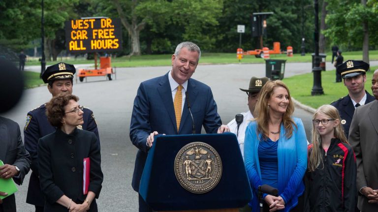 Mayor Bill de Blasio announced Thursday, June 18, 2015 that Central Park and Prospect Park will be mostly car free. The mayor made the announcement at the Bartel-Pritchard Square entrance to Prospect Park in Brooklyn. He is flanked by DOT Commissioner Polly Trottenberg, left, dark suit, and at right Sue Donoghue. Prospect Park Administrator and President of the Prospect Park Alliance.