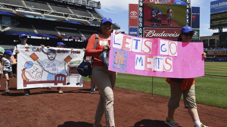 New York Mets fans walk with banners along the warning track at Citi Field on Banner Day before a baseball game between the Mets and the Atlanta Braves on Sunday, June 14, 2015.