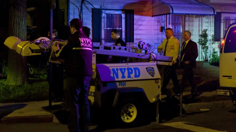 NYPD officers set up lights to search near homes and darkened alleys after a fellow officer was wounded by a gunman Saturday night, May 2, 2015, in Queens Village.