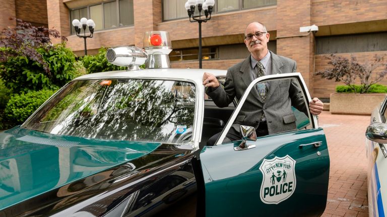 Michael Gorgia, Operations Supervisor, poses with a 1972 Plymouth Fury I, one of the vehicles in the NYPD's collection of vintage patrol cars.