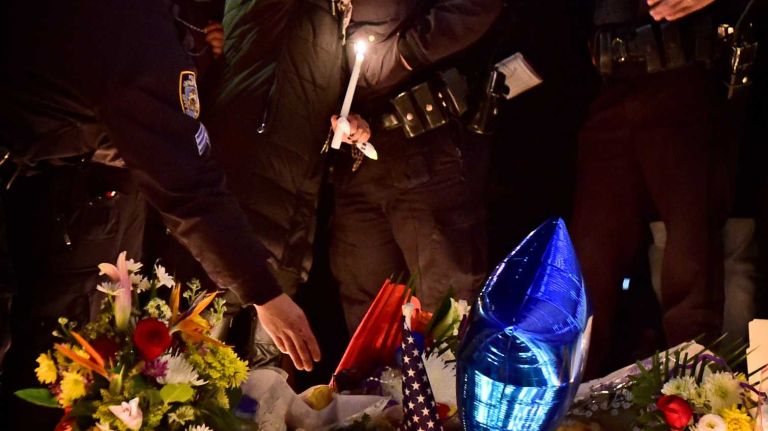 Police officers and mourners embrace on Sunday, Dec. 21, 2014, to light candles and pray at a memorial near the site of the shootings in Bedford-Stuyvesant. 