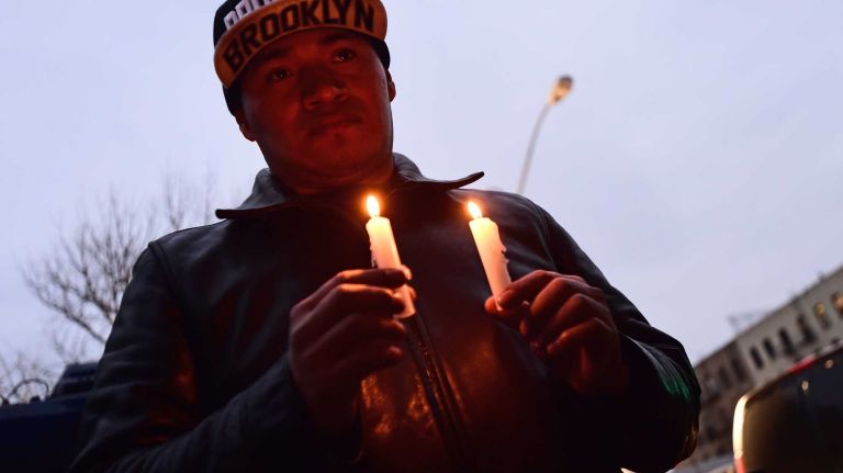 Adrien Esteven, of Brookyln, gathers to light candles and pray at a makeshift memorial in Bedford-Stuyvesant on Sunday, Dec. 21, 2014. 