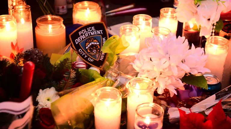 Candles and flowers are left at a memorial in Bedford-Stuyvesant on Sunday, Dec. 21, 2014, on the street where NYPD Officers Rafael Ramos and Wenjian Liu were killed a day before.