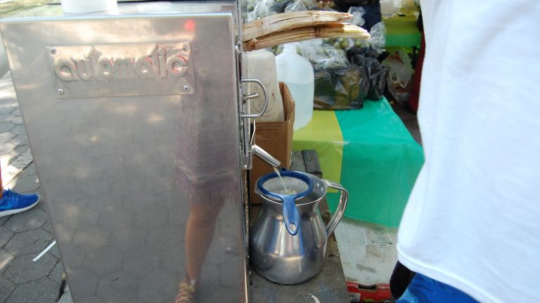 A man makes sugarcane juice out of raw sugarcane. Served over ice, the drink was refreshing out on the parkway. 