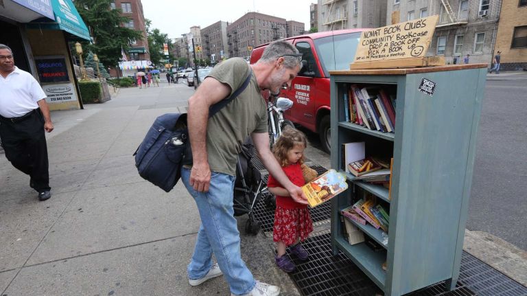Thor Wickstrom and daughter Irene browse through books at the Nomat Book Club's community bookcase on Broadway near 114th street in Inwood, Thursday, June 19, 2014. 