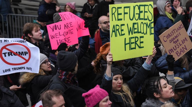 Protesters hold signs against the suspension of the country's refugee program at Kennedy Airport.