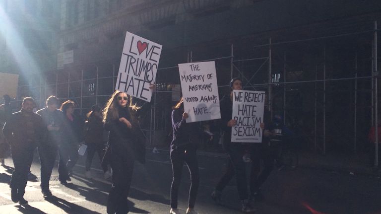 Demonstrators hold signs Saturday, Nov. 12, 2016, as they march to Trump Tower showing their thoughts on stated policies of President-elect Donald Trump.