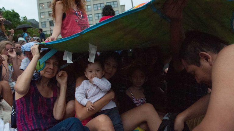 People wait in the rain to watch the Macy's 4th of July Fireworks from Brooklyn Bridge Park on July 4, 2016.