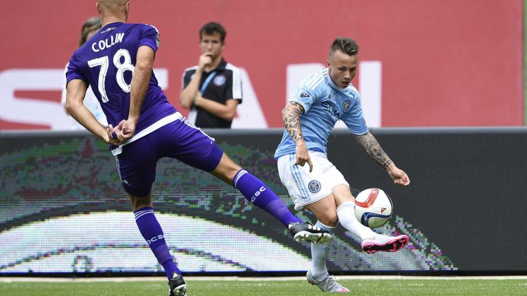 New York City FC defender Angelino (69) sends the ball in toward the goal under pressure from Orlando City FC defender Aurelien Collin (78) in an MLS game at Yankee Stadium on Sunday, July 26, 2015.