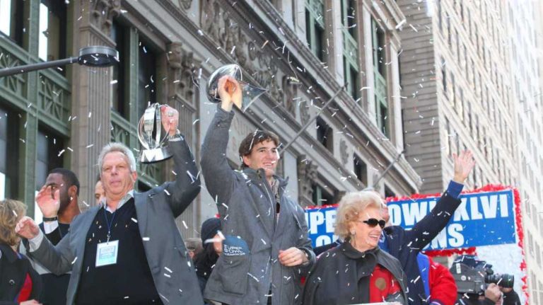 New York Giants owner Stephen Tisch, left, and quarterback Eli Manning hoist the team's trophies as their float moves through the Canyon of Heroes on Broadway heading toward City Hall during a victory ticker-tape parade. (Feb. 7, 2012) 