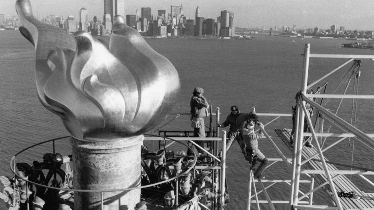 Workers remove scaffolding from around the torch of the Statue of Liberty, with the Manhattan skyline and the twin towers of the World Trade Center in the background. (Dec. 17, 1985)