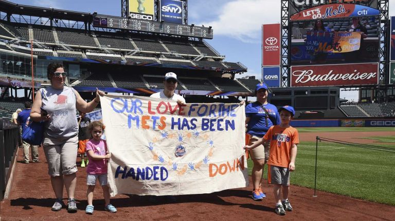 New York Mets fans walk with banners along the warning track at Citi Field on Banner Day before a baseball game between the Mets and the Atlanta Braves on Sunday, June 14, 2015.