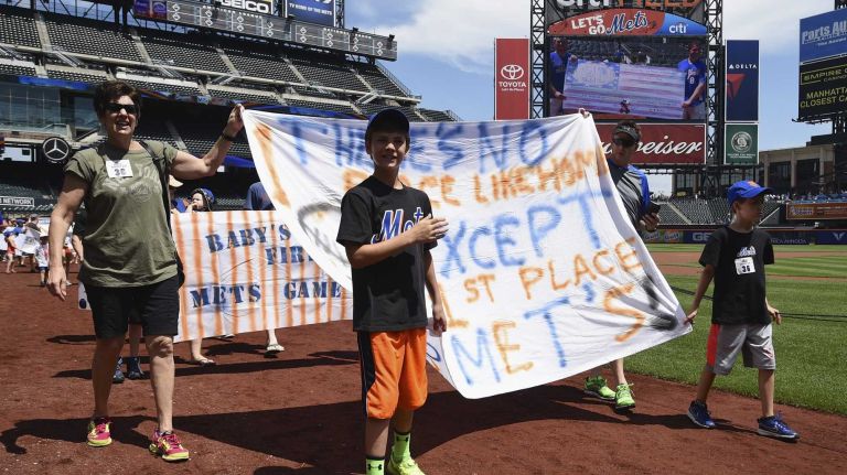 New York Mets fans walk with banners along the warning track at Citi Field on Banner Day before a baseball game between the Mets and the Atlanta Braves on Sunday, June 14, 2015.