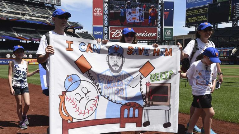 New York Mets fans walk with banners along the warning track at Citi Field on Banner Day before a baseball game between the Mets and the Atlanta Braves on Sunday, June 14, 2015.