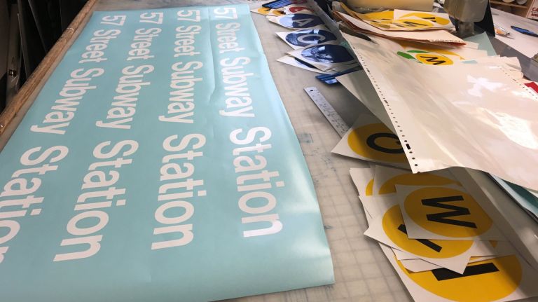 A sign fabricator's desk is covered in rulers, subway bullets and transfer paper. Sign fabricators make their signs mostly by hand.
