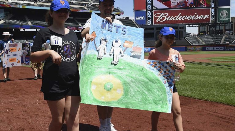 New York Mets fans walk with banners along the warning track at Citi Field on Banner Day before a baseball game between the Mets and the Atlanta Braves on Sunday, June 14, 2015.