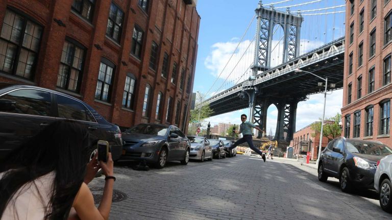 Newlyweds, Jieun Kim and Geon Heo, from Korea, stop along Washington Street to photograph one another with the Manhattan Bridge in the background in Dumbo on June 6, 2014.
