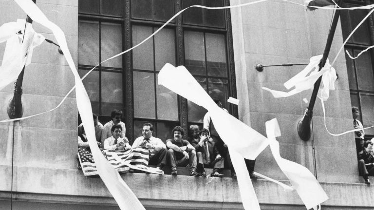 Office workers sit on the ledge of buildings several stories above the parade honoring Vietnam veterans as they proceed down the Canyon of Heroes on Broadway in lower Manhattan. (May 7, 1985)