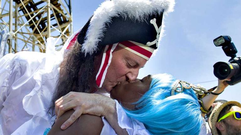 Chirlane McCray and her husband Mayor Bill de Blasio kiss near the Cyclone roller coaster as they march in the annual Coney Island Mermaid Parade Saturday, June 21, 2014.