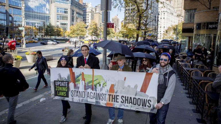 New Yorkers carry black umbrellas near Columbus Circle in Manhattan to symbolize the huge shadows the towers cast throughout the day across emblematic sections of Central Park on Sunday, Nov. 8, 2015. 