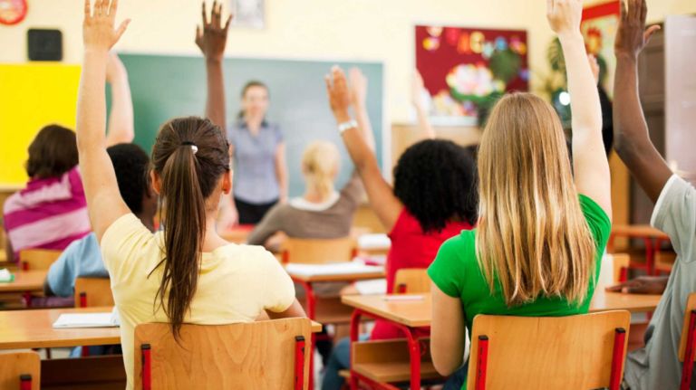 This file image shows teens sitting in a classroom and raising hands to answer aquestion.