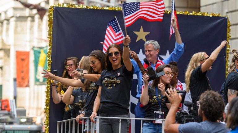 U.S. Women's National Team member Alex Morgan waves to the crowd with Mayor Bill de Blasio behind her.&nbsp;