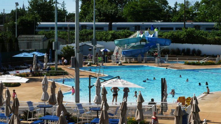 A LIRR train passes within feet of the Floral Park pool's water slide Tuesday, June 14, 2016. The Village of Floral Park is concerned that a proposed third track for the LIRR line that runs next to the community's pool and recreation complex will have a negative impact on the village.